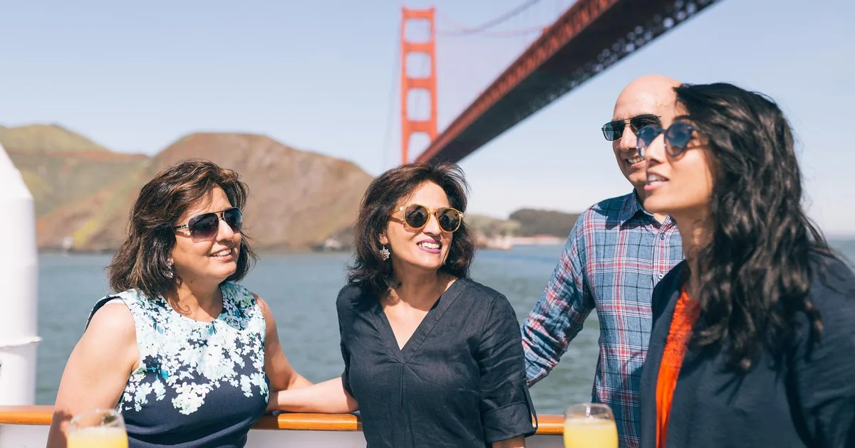 Four guests with glasses of mimosa on the deck of a City Cruises boat beneath the Golden Gate Bridge on a sunny day