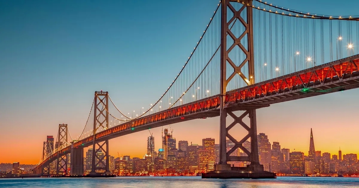 The Bay Bridge lit up at dusk with the San Francisco skyline behind it, seen from the water