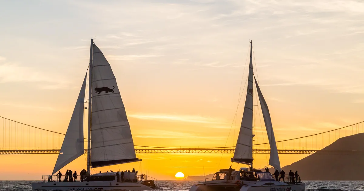 Two sailing catamarans silhouetted against the sunset with the Golden Gate Bridge behind them